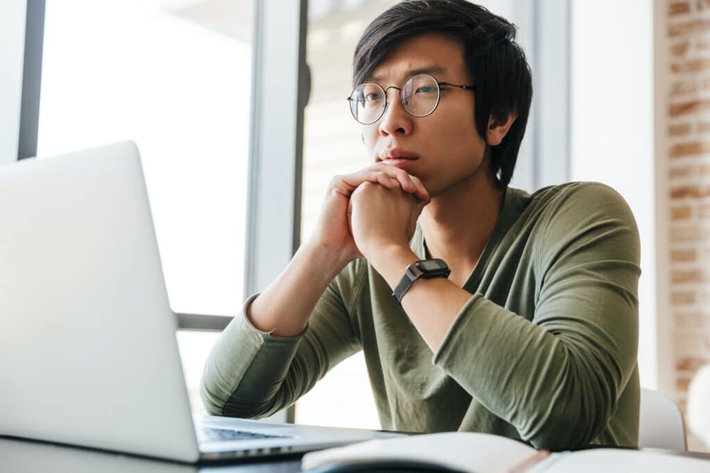 Image of handsome young asian man using laptop in apartment